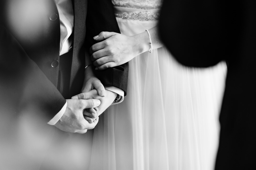close up of bride and groom holding hands during wedding ceremony
