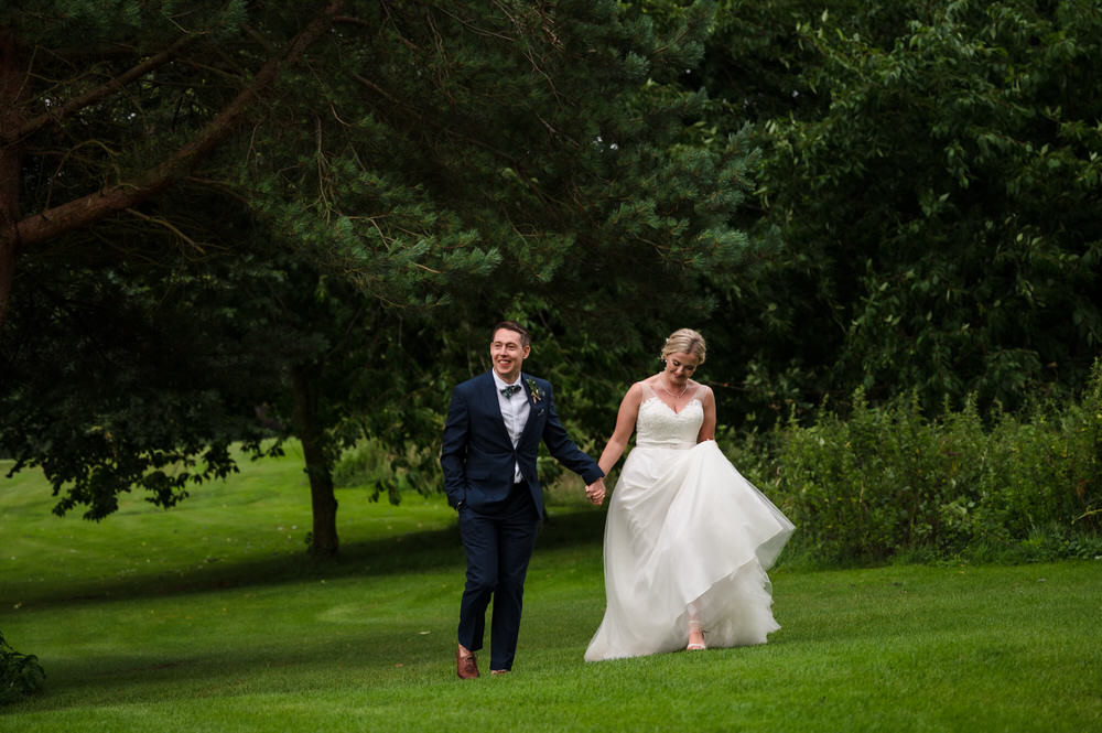 bride and groom holding hands and walking through the grass