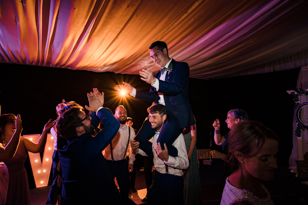 groom on his friends shoulders at wedding on dancefloor