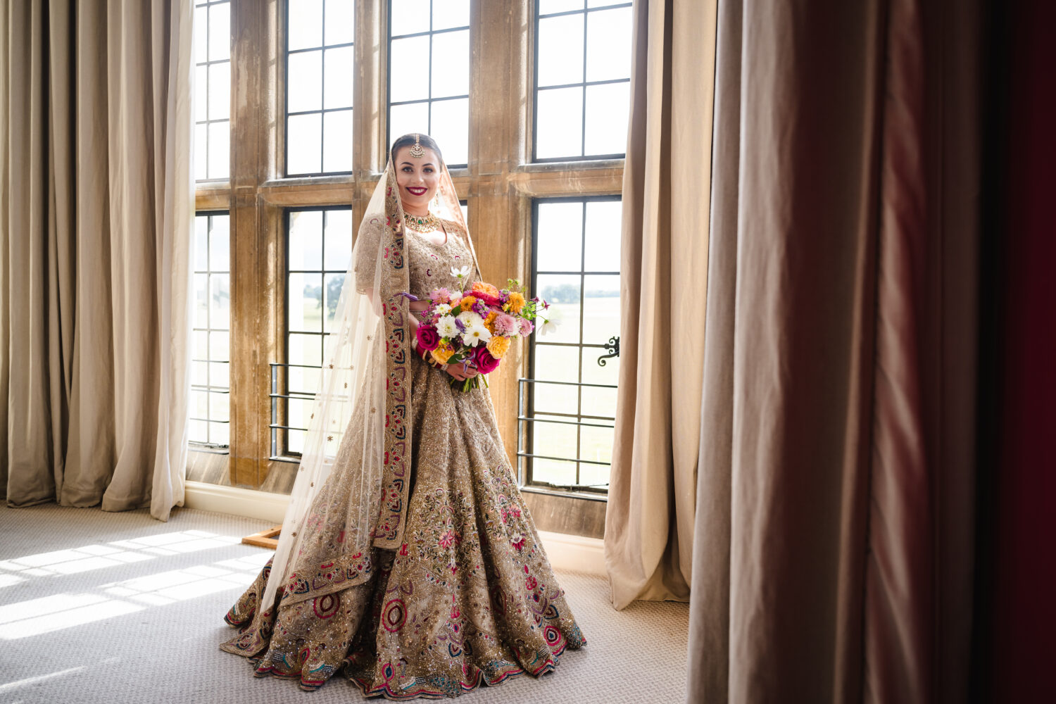 Bride stood in the window with her bright bouquet at stapleford park