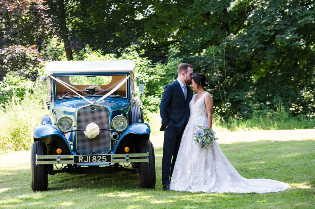 bride and groom stood next to their vintage blue wedding car