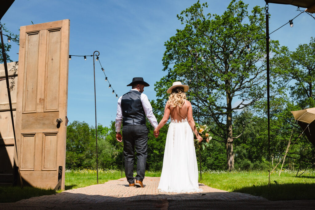 bride and groom wlaking away from tipi at dibbins wood wearing cowboy hats